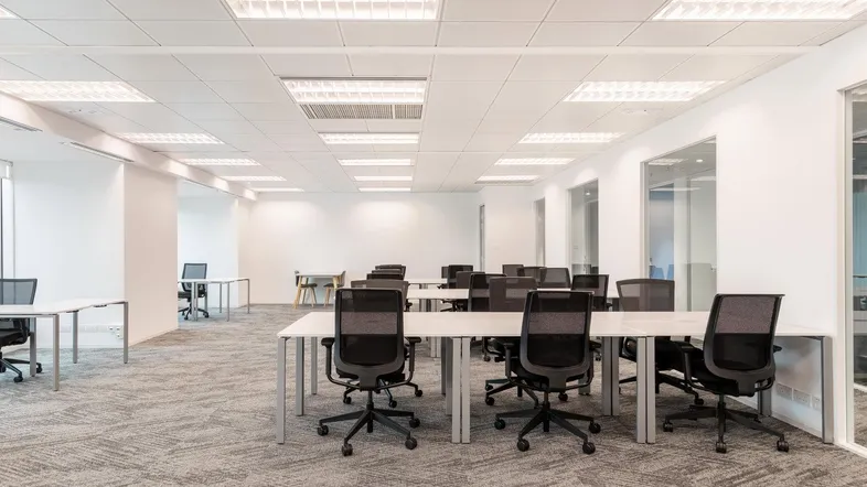 Großes, offenes Büro mit zahlreichen Schreibtischen, Bürostühlen und Teppichboden, ideal für Teamarbeit.