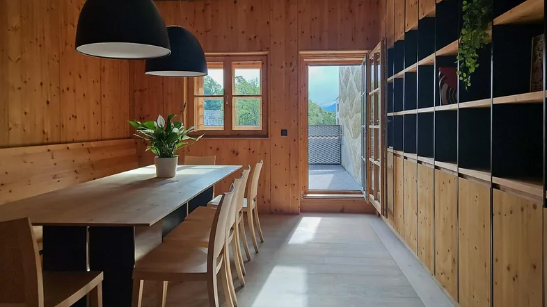Geräumiger Essbereich mit Holztäfelung, langem Holztisch und Zugang zu einem Balkon mit Bergblick.