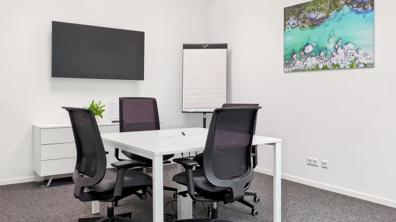 Moderner Besprechungsraum mit weißem Tisch, ergonomischen Stühlen und einem Wandbild, ideal für produktive Meetings.