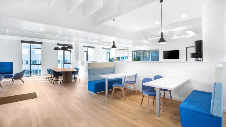 Moderner Bürobereich mit verschiedenen Sitzgelegenheiten, Tischen und großen Fenstern, ideal für Pausen und informelle Treffen.