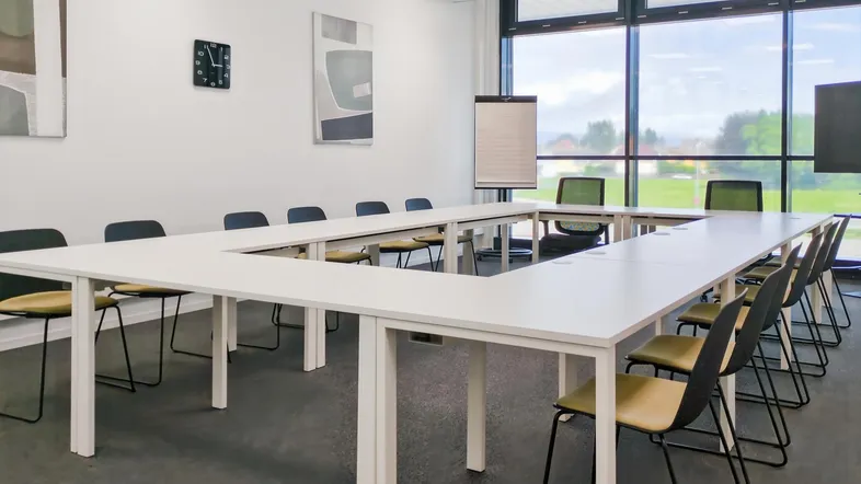 Großer Konferenzraum mit U-förmiger Tischordnung, großen Fenstern und Blick ins Grüne.
