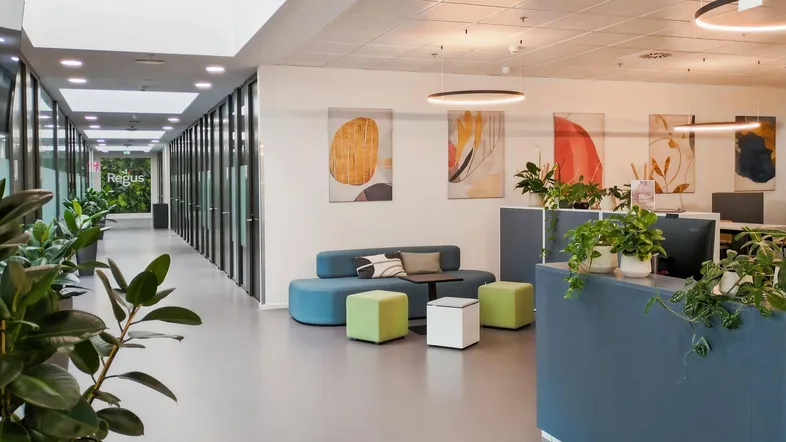 Moderner Bürobereich mit Empfangstheke, Lounge-Sitzgelegenheiten und einem hellen Flur mit vielen Pflanzen.