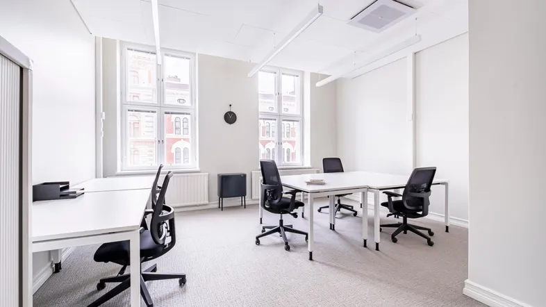 Helles, modernes Büro mit mehreren Arbeitsplätzen, großen Fenstern und Teppichboden in einem gepflegten Gebäude.