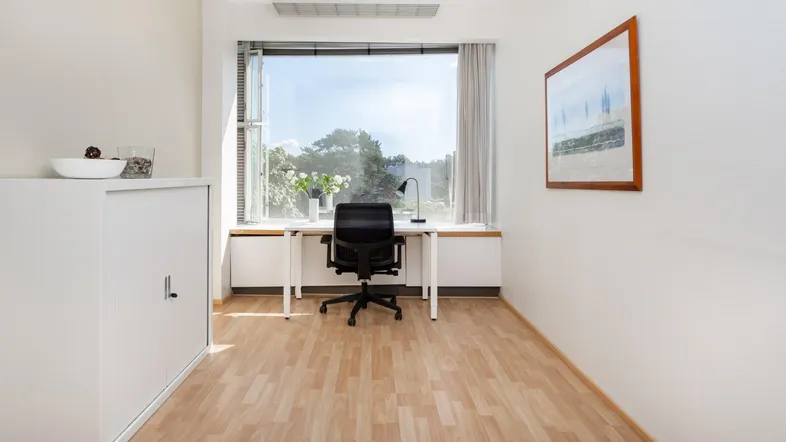 Helles Büro mit Holzboden, großem Fenster und Blick ins Grüne, ideal für konzentriertes Arbeiten.