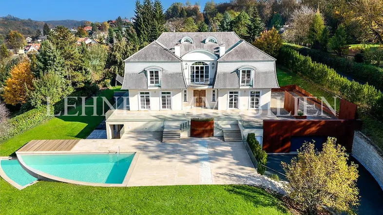 Eindrucksvolle Villa mit großem Garten, Swimmingpool und weitläufiger Terrasse unter blauem Himmel.
