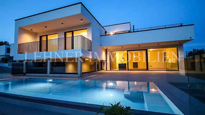 Moderne Villa bei Nacht mit beleuchtetem Pool und großzügiger Terrasse.