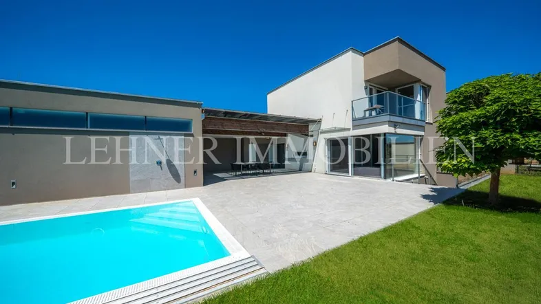 Moderne Villa mit großem Pool, gepflegtem Rasen und weitläufiger Terrasse unter blauem Himmel.