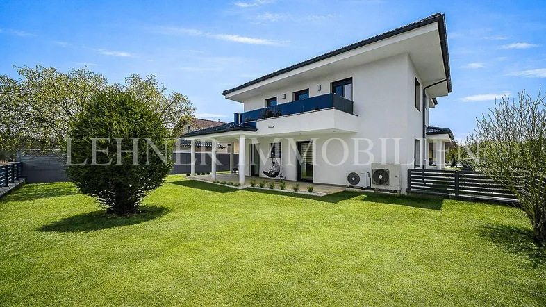 Modernes Einfamilienhaus mit weißer Fassade, großem Garten und überdachter Terrasse.