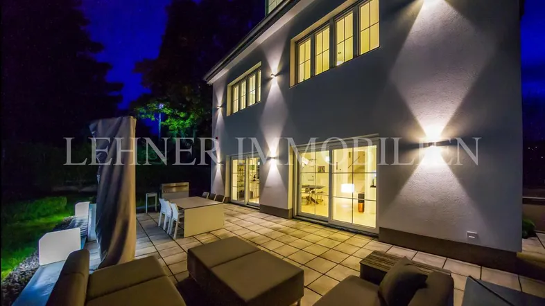 Große, beleuchtete Terrasse mit modernen Lounge-Möbeln und Esstisch, ideal für Abendstunden.