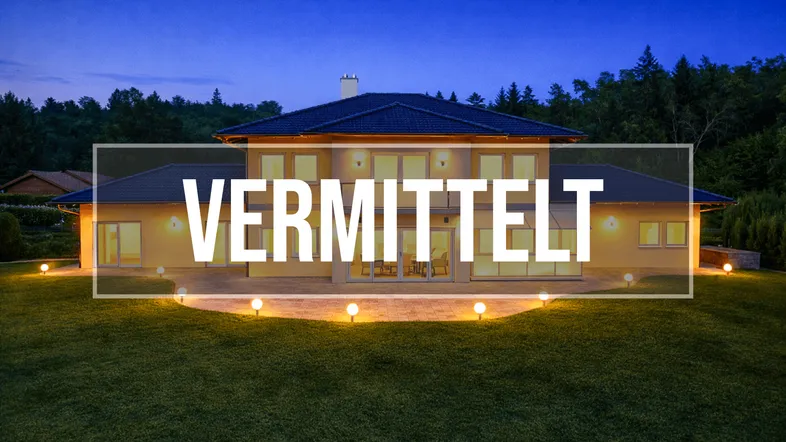 Modernes Einfamilienhaus bei Dämmerung mit beleuchtetem Garten und der Aufschrift 'VERMITTELT'.