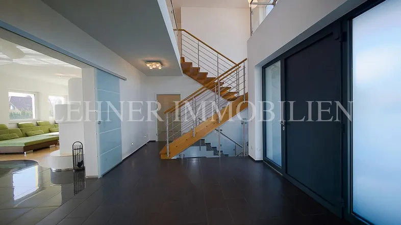 Moderner Eingangsbereich mit dunklem Fliesenboden, offener Treppe und Blick ins Wohnzimmer.
