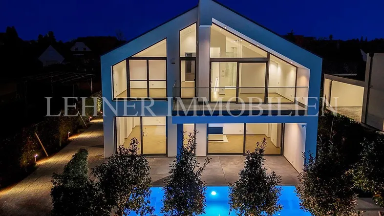 Moderne Villa bei Nacht mit beleuchtetem Pool und großen Glasfronten, die den Innenraum zeigen.