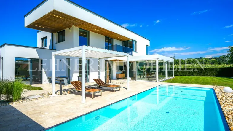 Moderne Villa mit großem Pool, Sonnenterrasse und gepflegtem Garten unter blauem Himmel.