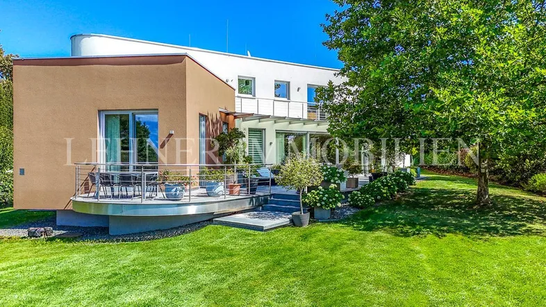 Moderne Villa mit weitläufiger Terrasse, umgeben von einem gepflegten Garten und altem Baumbestand.