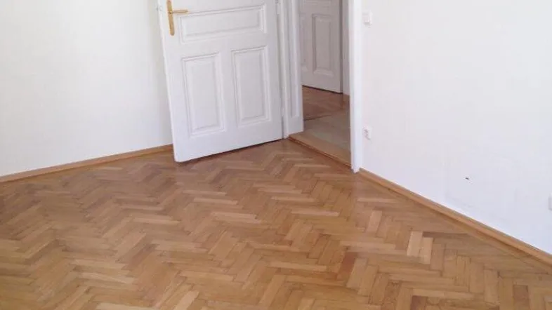 Heller Raum mit Fischgrätparkettboden und weißer Flügeltür, die zu einem weiteren Zimmer führt.