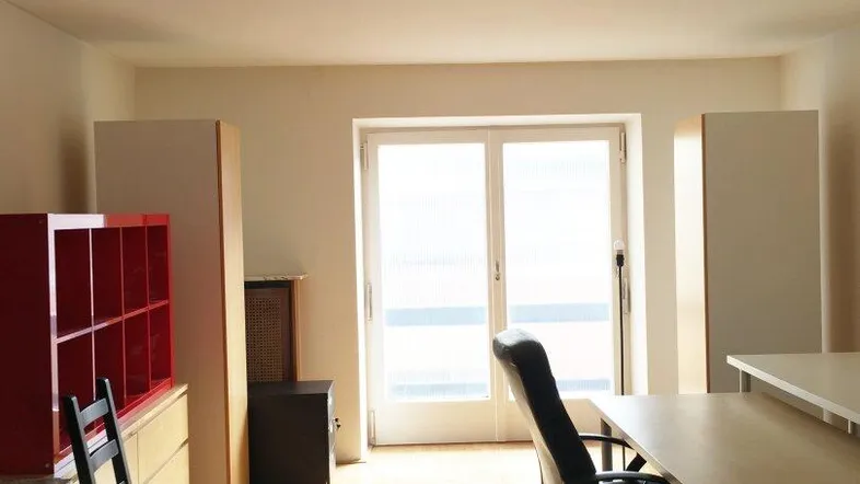 Helles Zimmer mit Parkettboden, Stuckdecke und Zugang zu einem Balkon, ideal als Wohn- oder Arbeitsbereich.
