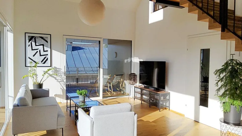 Helles Wohnzimmer mit hohen Decken, Holzboden und Zugang zu einer sonnigen Terrasse.