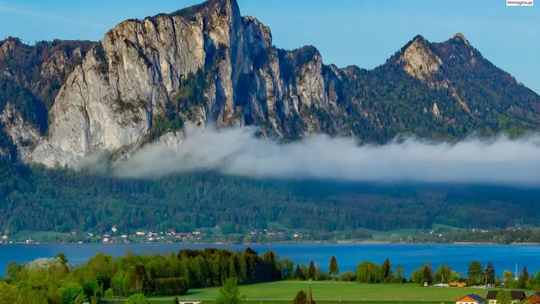 Malerische Landschaft mit majestätischen Bergen, einem ruhigen See und vereinzelten Häusern am Ufer.