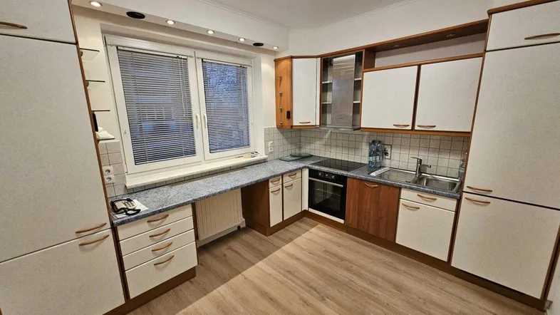 Funktionale Küche mit Laminatboden, Fenster und Einbauschränken in Holz- und Weißtönen.