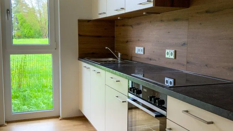 Moderne Einbauküche mit hellen Fronten, dunkler Arbeitsplatte und Blick ins Grüne durch das Fenster.