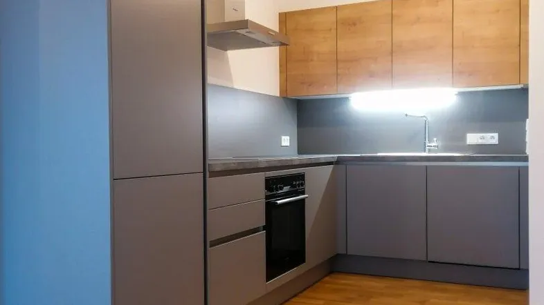 Moderne Einbauküche in Grau mit Holzakzenten und integrierten Geräten, bereit zur ersten Nutzung.