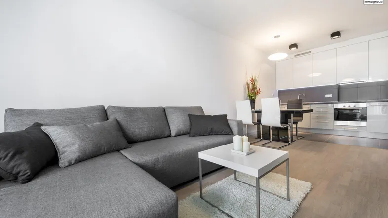 Moderner offener Wohn- und Essbereich mit grauer Couch und integrierter Küche.