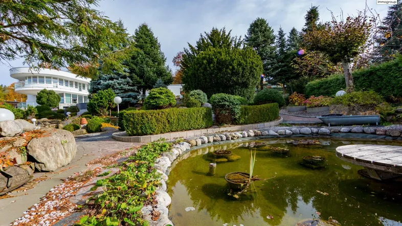 Idyllischer Gartenbereich mit einem dekorativen Teich und üppiger Bepflanzung, umgeben von Bäumen.