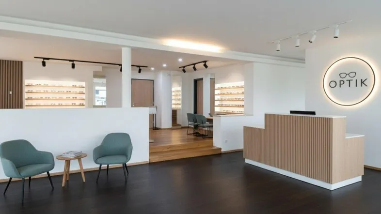 Moderner Empfangsbereich eines Optikergeschäfts mit dunklem Holzboden und stilvoller Beleuchtung.