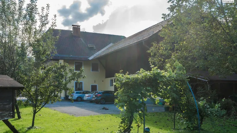 Gelbes Gebäude mit traditionellem Dach, umgeben von Bäumen und Grünflächen, mit Parkplätzen auf dem Grundstück.