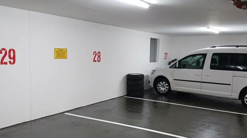 Helle Tiefgarage mit markierten Stellplätzen und einem geparkten Fahrzeug in gutem Zustand.