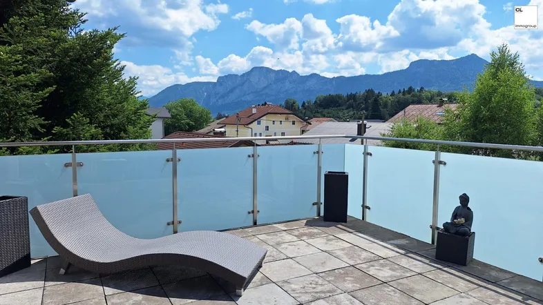 Geräumige Terrasse mit Liegestuhl und Glasgeländer, bietet einen weiten Blick auf die Berge.