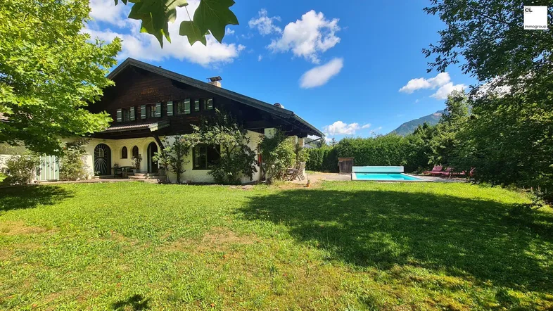 Großzügiger Gartenbereich mit Rasenfläche, Pool und Blick auf das traditionelle Haus im Alpenstil.