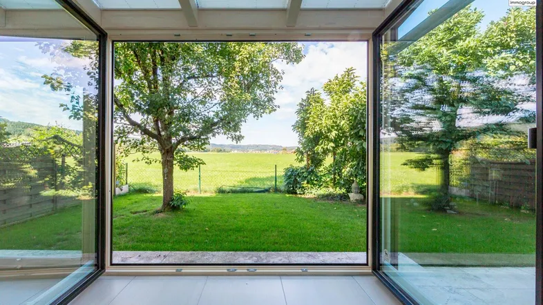 Heller Wintergarten mit großen Glasfronten und weitem Blick ins Grüne und die Landschaft.