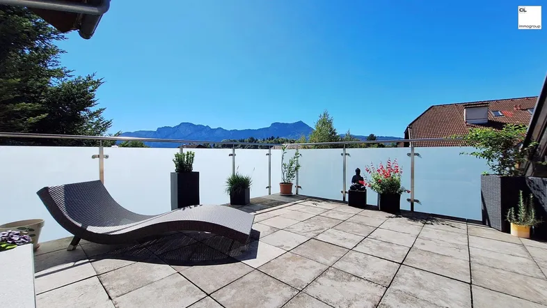 Große geflieste Terrasse mit Liegestuhl, Pflanzen und weitem Bergblick unter blauem Himmel.