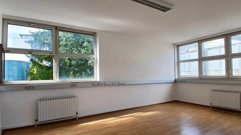 Heller Büroraum mit großen Fenstern, Holzboden und Heizkörpern, ideal für verschiedene Nutzungsmöglichkeiten.