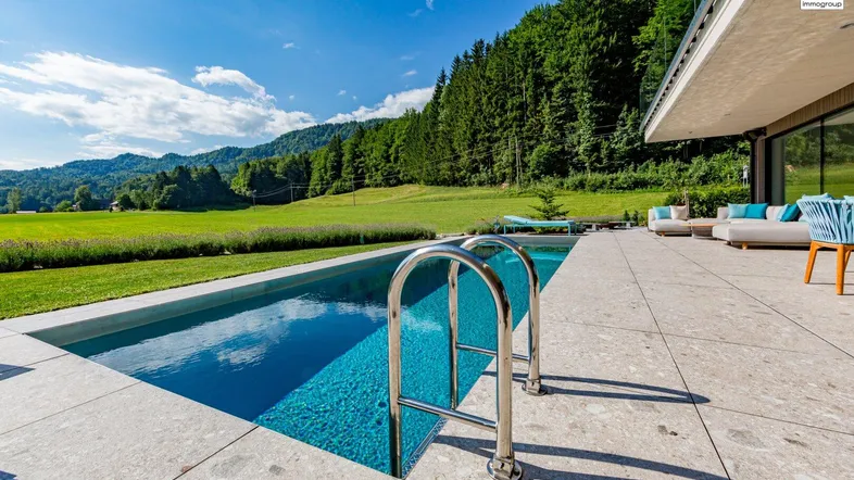 Moderner Außenpool mit großzügiger Terrasse und weitem Blick auf die grüne Landschaft und Berge.