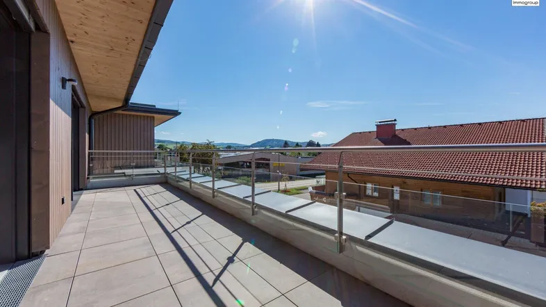 Sonniger Balkon mit Glasgeländer und weitem Blick auf die umliegende Landschaft und Berge.