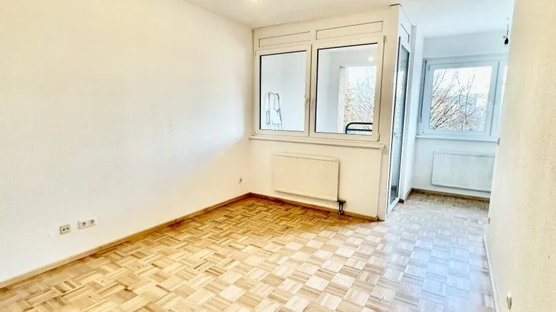 Helles Wohnzimmer mit Fischgrätparkettboden und großen Fenstern, bereit zur individuellen Gestaltung.