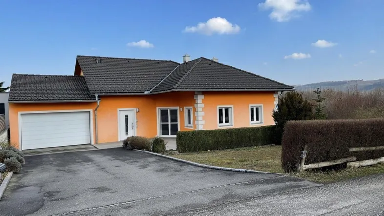 Einfamilienhaus mit orangefarbener Fassade, Garage und gepflasterter Auffahrt unter blauem Himmel.