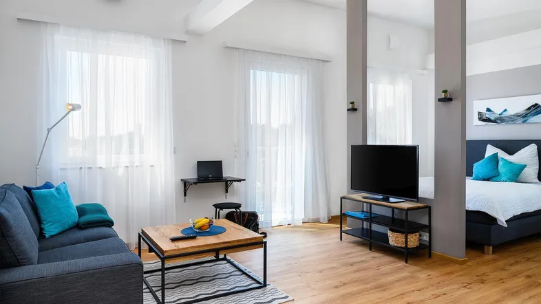 Helles Wohnzimmer mit Holzboden, bequemer Couch und offenem Schlafbereich.
