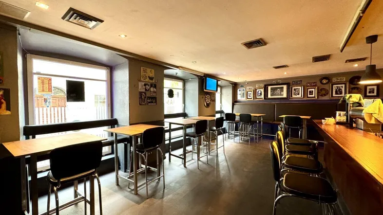 Geräumiger Innenbereich einer Bar mit Tischen, Stühlen und einer Theke, gut beleuchtet durch Fenster.