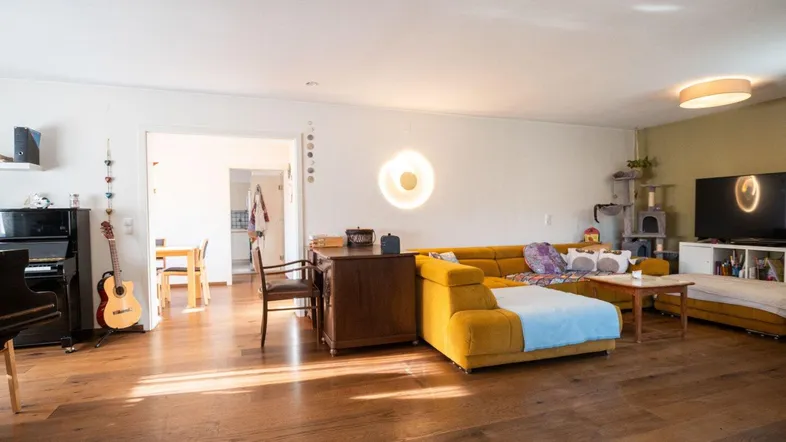 Offener Wohnbereich mit gelbem Sofa, Holzboden und direktem Zugang zur Küche.
