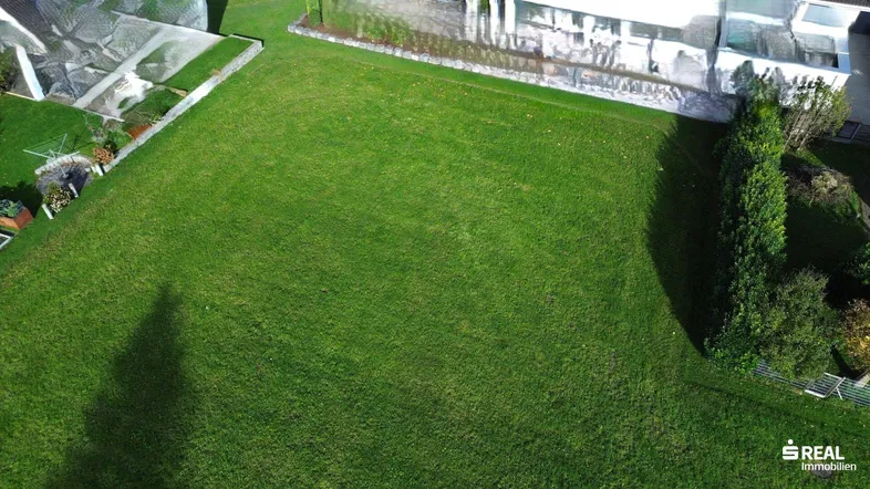 Luftaufnahme eines großen, gepflegten Rasengrundstücks mit umliegenden Gebäuden und viel Grün.