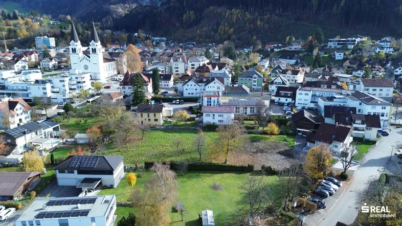 Luftaufnahme einer malerischen Stadt mit Kirche, Wohngebäuden und grünen Hügeln im Hintergrund.