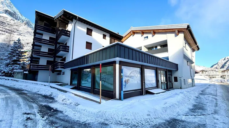 Das Gebäude präsentiert sich im Winter mit verschneiter Umgebung und klarem Himmel, umgeben von Bergen.