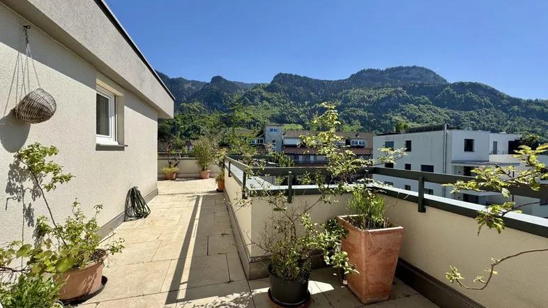 Geräumige Dachterrasse mit Fliesenboden, Topfpflanzen und einem weiten Blick auf die umliegenden Berge.
