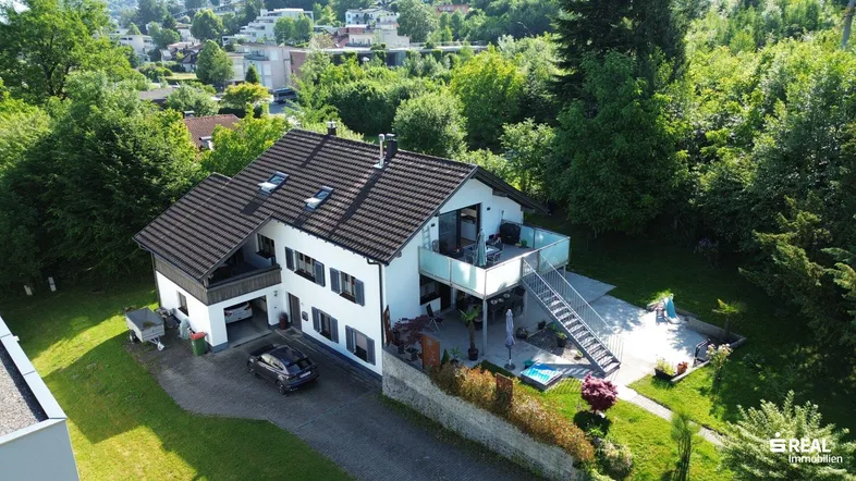 Luftaufnahme des Einfamilienhauses mit Garten, Balkonen und umliegender grüner Landschaft.