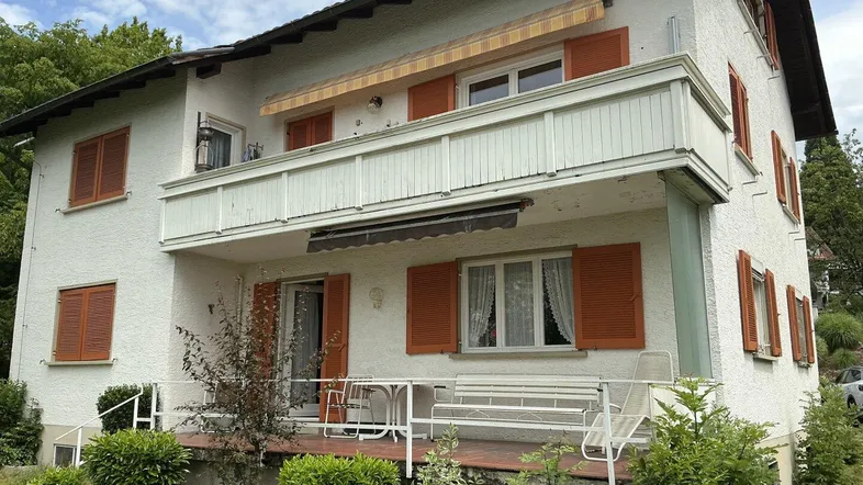 Rückseite des Hauses mit großem Balkon, Markise und einer Terrasse mit Gartenmöbeln.