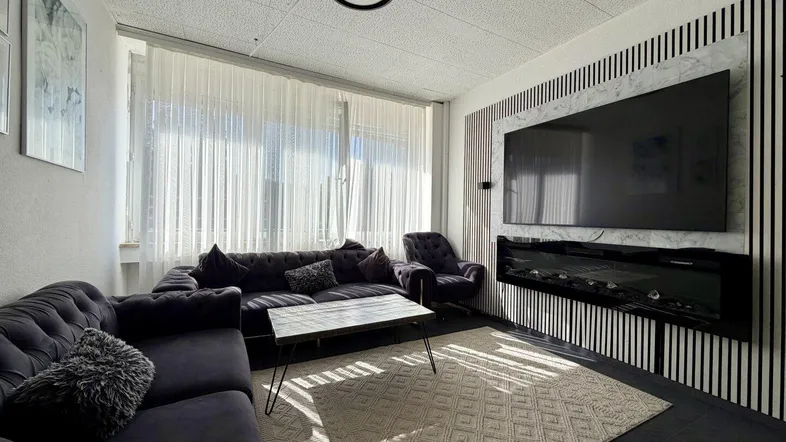 Gemütliches Wohnzimmer mit großer Couch, modernem TV-Bereich und viel Tageslicht durch große Fenster.