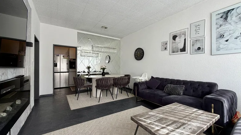Moderner Wohn-Essbereich mit dunklem Boden, bequemer Couch und elegantem Esstisch, teilweise verspiegelt.